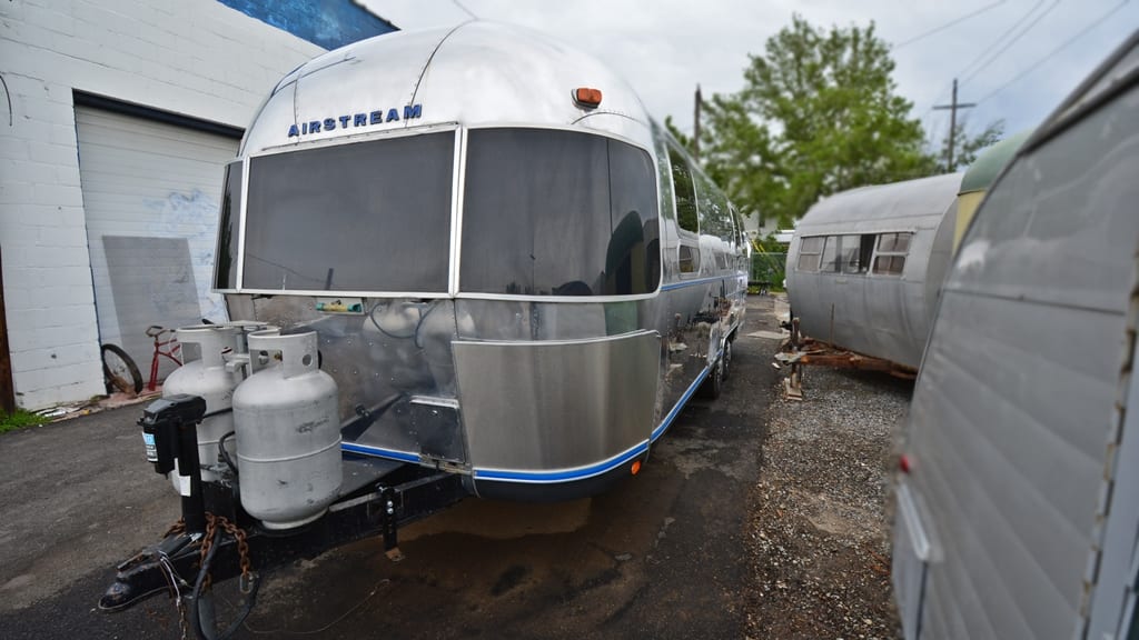 Front exterior view with dual propane tanks, polished aluminum body, and custom blue trim on 1971 Airstream Sovereign