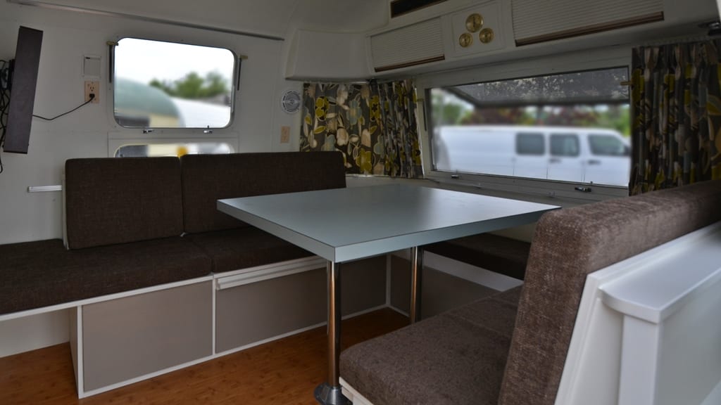 Brown upholstered dinette seating with center table, laminate cabinetry, and patterned curtains in 1971 Airstream Sovereign