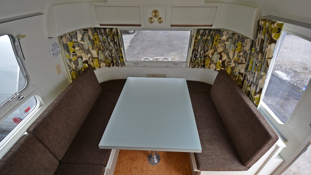 Dinette with brown upholstered benches, frosted glass table, floral curtains, and bamboo flooring, 1971 Airstream Sovereign