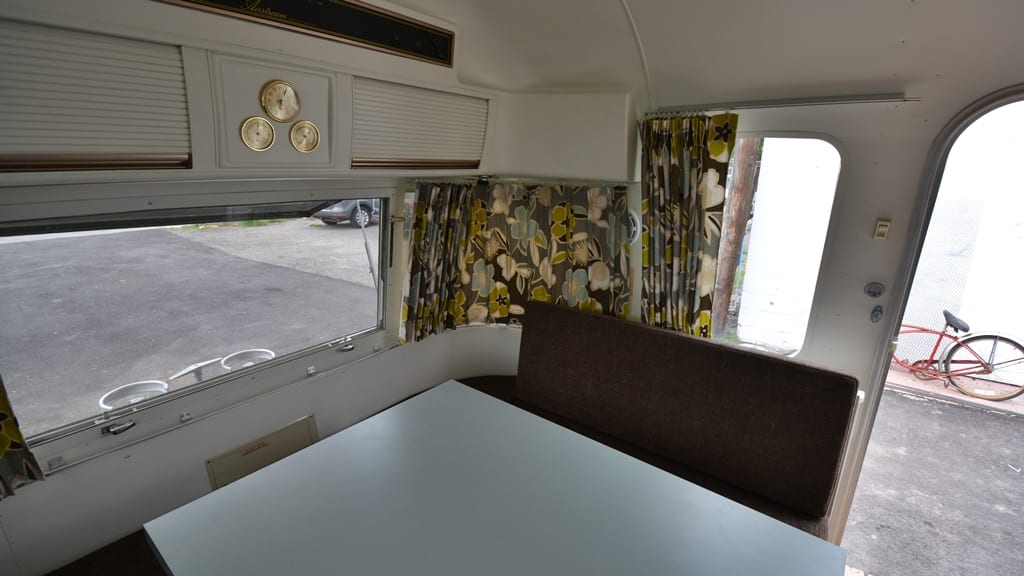 Dinette area with brown bench seating, floral curtains, wall-mounted gauges, and large window in 1971 Airstream Sovereign
