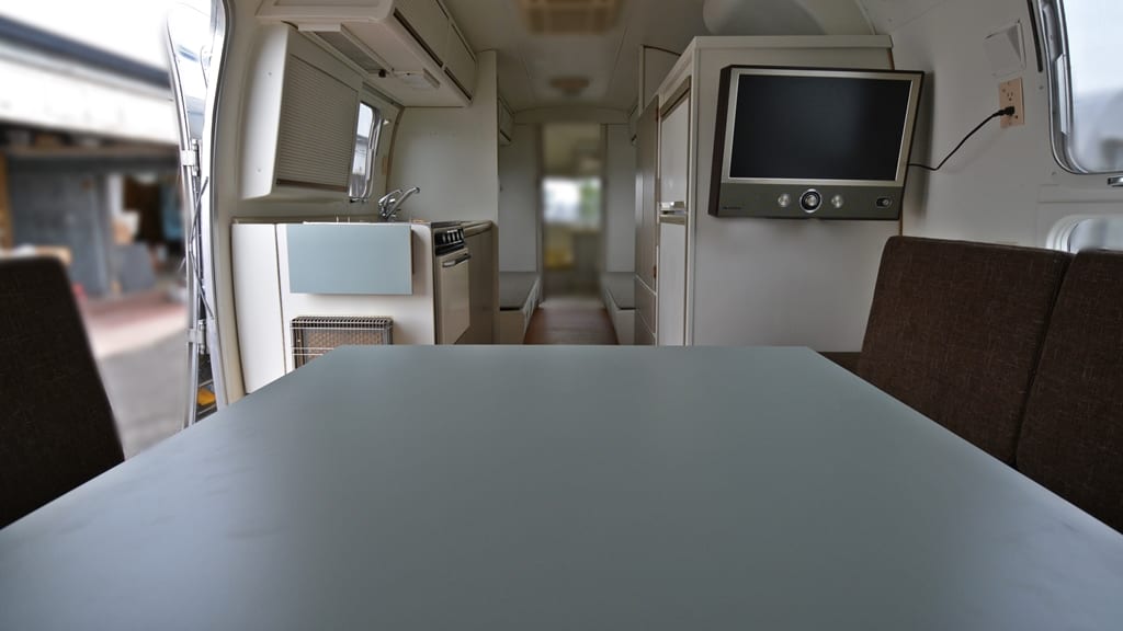 Dining table with brown bench seating, wall-mounted TV, compact kitchen with sink and stove inside 1971 Airstream Sovereign
