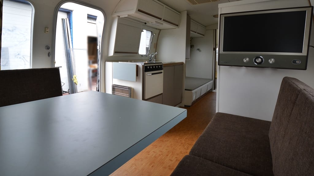 Fold-down table, dual bench seats, wall-mounted TV, compact kitchenette with stove and sink in 1971 Airstream Sovereign