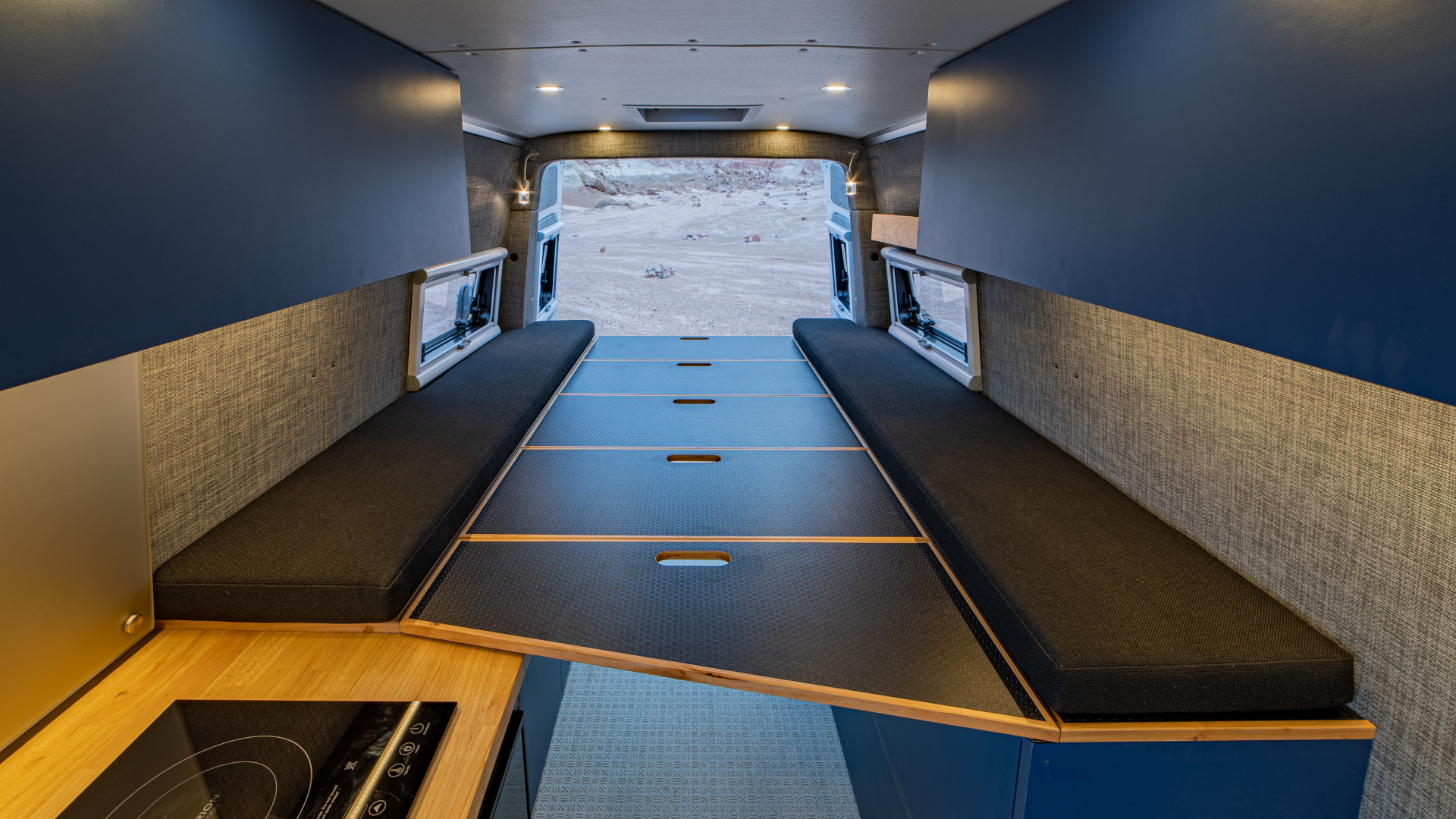 Convertible sleeping platform with black cushions, overhead storage, and fold-out panels in rear interior 2021 Sprinter 4x4 VS30.