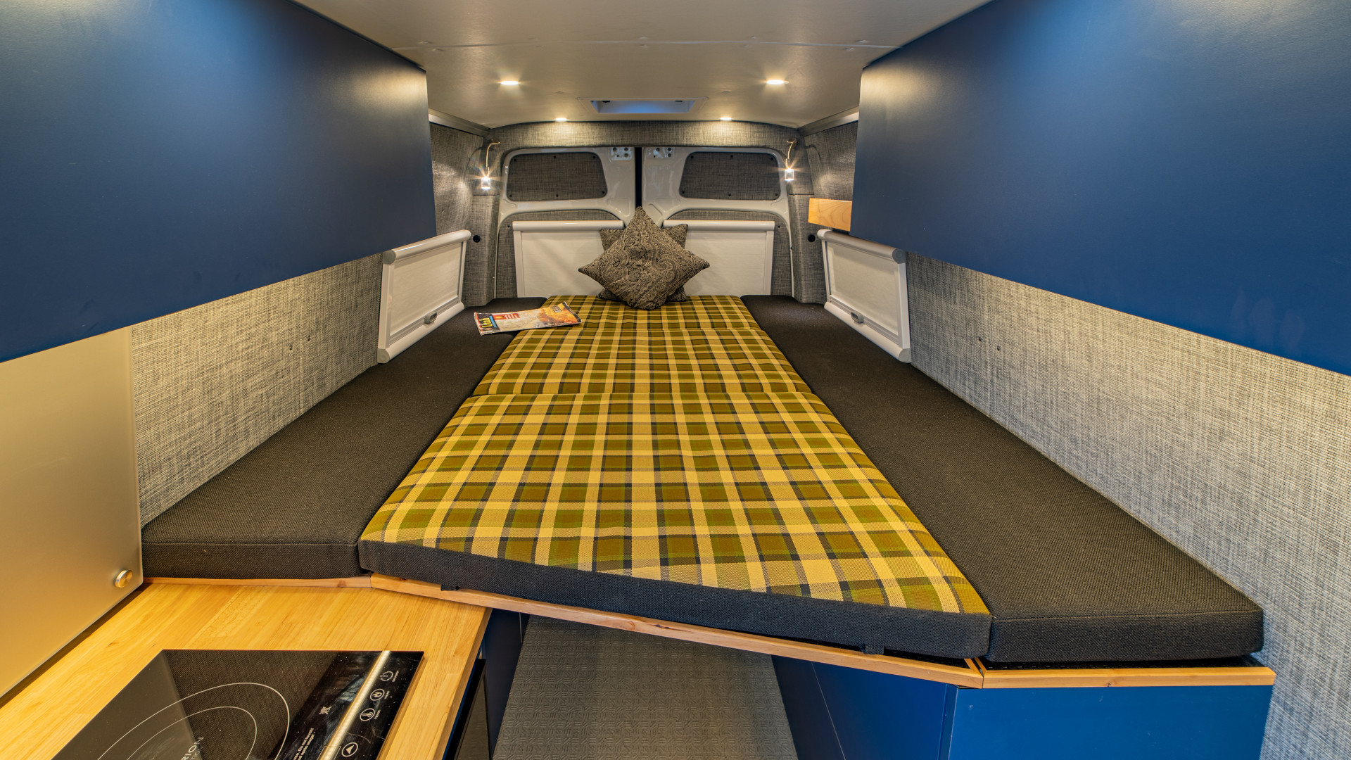 Plaid fold-out bed with surrounding bench cushions, overhead lighting, and built-in storage compartments, 2021 Sprinter 4x4