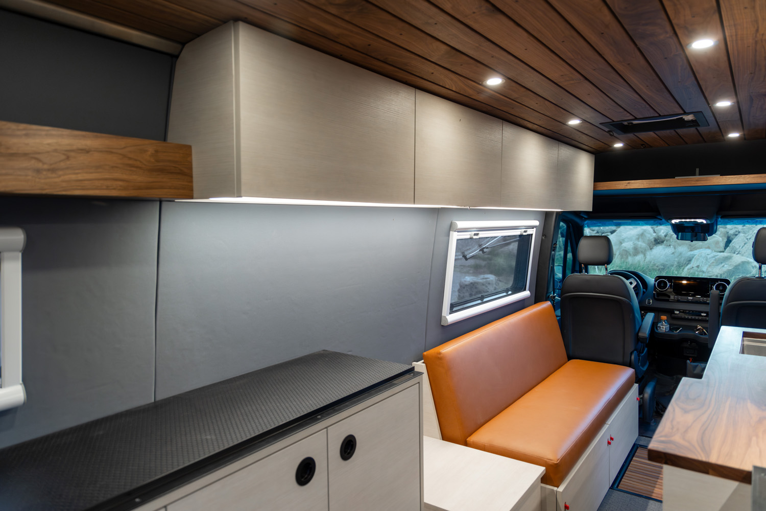 Overhead cabinets, wood-paneled ceiling with recessed lighting, leather bench seat, and compact window shade system, 2022 Sprinter 170