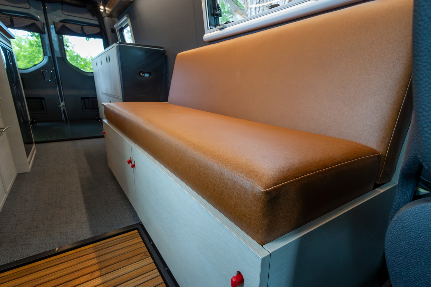 Padded tan bench seat with integrated storage drawers and red latches inside converted van interior, 2022 Sprinter 170 Adventure Van